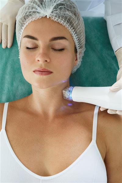 زن زیبا در حین درمان لیفت با فرکانس رادیویی روی گردن خود در یک کلینیک زیبایی پزشکی