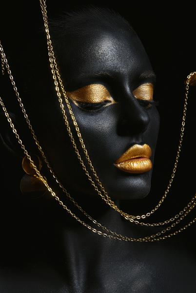 زن زیبایی با رنگ پوست مشکی نقاشی شده است زنجیر طلایی در دستان و دور گردنش آرایش طلایی لب پلک ناخن نوک انگشتان در رنگ طلایی آرایش حرفه ای