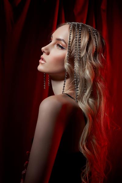 زن بلوند زیبا با موهای بلند در زمینه مخملی قرمز جواهرات مو روی سر یک زن آرایش مدرن و تیرهای روی چشم