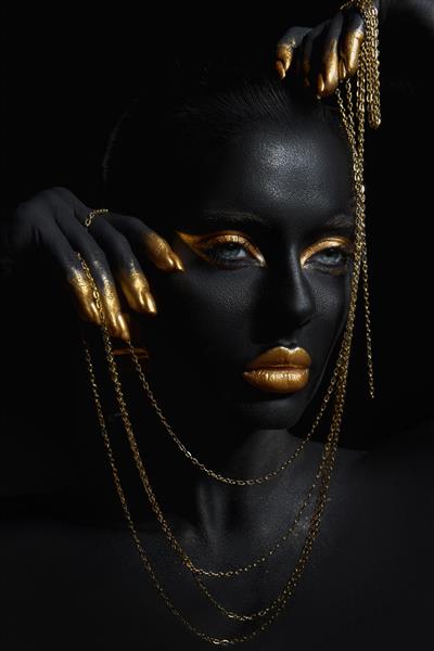زن زیبایی با رنگ پوست مشکی رنگ شده با زنجیر طلایی در دست و دور گردنش آرایش طلایی لب پلک انگشتان ناخن به رنگ طلایی رنگ آرایش حرفه ای