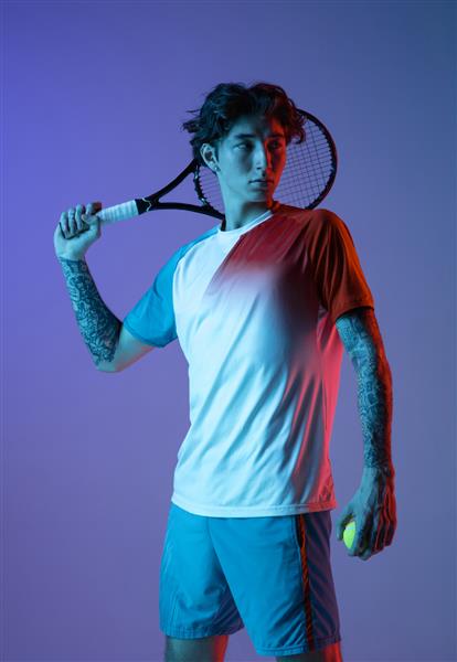مرد جوان قفقازی در حال بازی تنیس جدا شده روی پس‌زمینه استودیو آبی بنفش در مفهوم اکشن و حرکت نئون