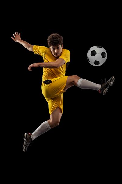 پرتره فوتبال مرد جوانی که در تمرین حرکتی بازی می‌کند جدا شده از پس‌زمینه سیاه استودیویی که به توپ ضربه می‌زند