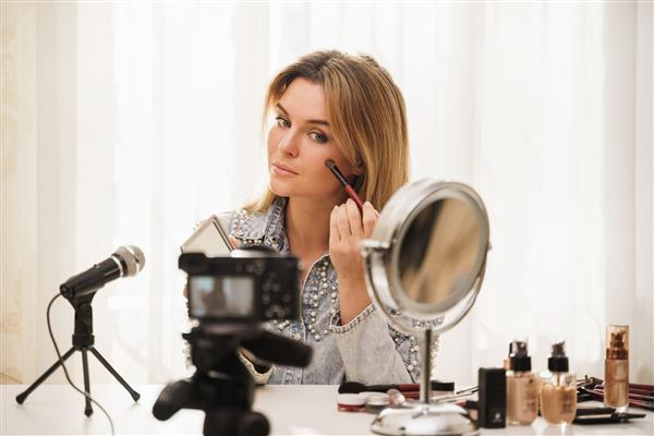 زن وبلاگ نویس زیبایی در حال استفاده از رژگونه روی صورت خود در حین ضبط ویدیوی آموزشی برای فالوورهایش