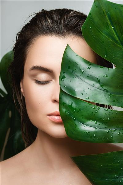 زن جوان با پوستی صاف که برگ گیاه مونسترا دلیسیوزا را در دست گرفته است