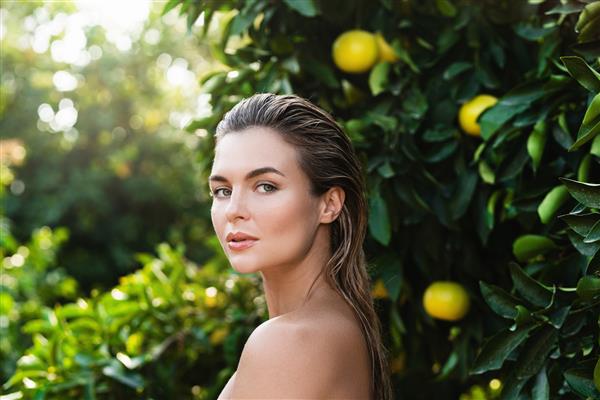 پرتره زن زیبا با پوست صاف در برابر درختان لیمو