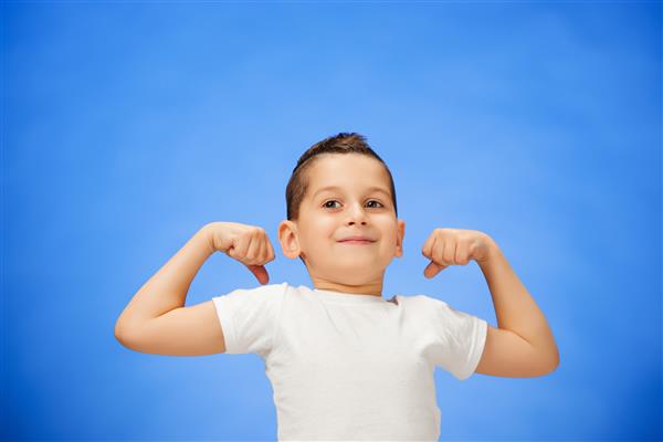 پسر بچه ورزشی خندان زیبایی که عضله دوسر خود را نشان می دهد