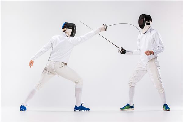 دو مرد با لباس شمشیربازی در حال تمرین با شمشیر در برابر خاکستری