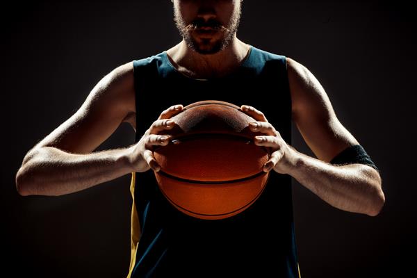 نمای سیلوئت یک بسکتبالیست که توپ سبد را در فضای سیاه نگه داشته است
