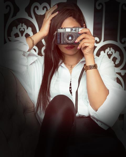 مدل دختر زیبا با موهای بلند سیاه و بلوز سفید و دوربین عکاسی در دستانش