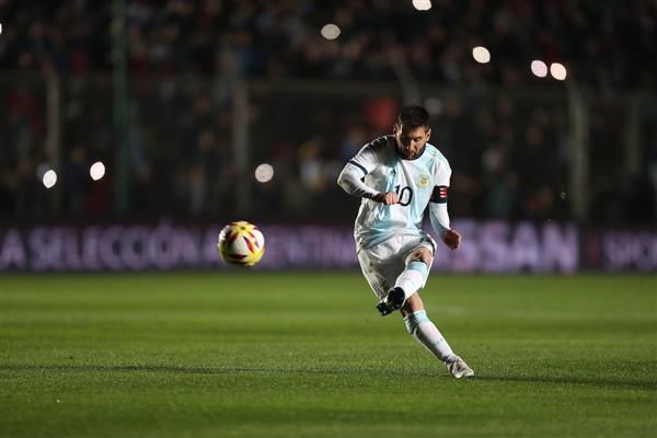لیونل مسی در زمین فوتبال با پیراهن تیم آرژانتین در حال ضربه زدن به توپ فوتبال
