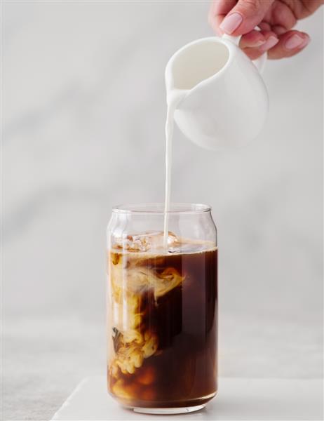 قهوه سرد در یک لیوان بلند با خامه ریخته روی آن قهوه سیاه سرد با تکه های یخ در یک خامه بریز شیشه ای بالا