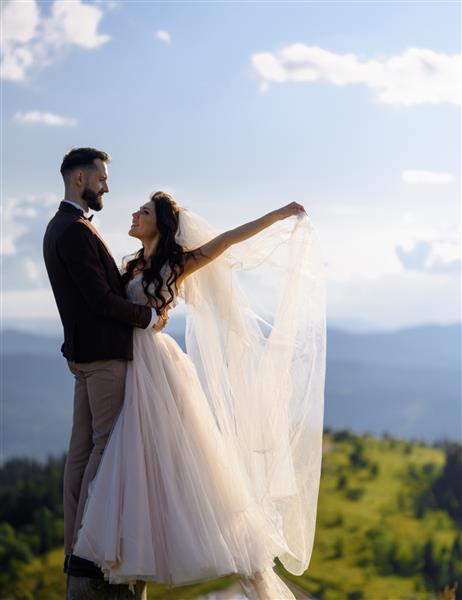 زوج عاشق با لباس عروسی که در طبیعت در کوهستان ژست گرفته اند