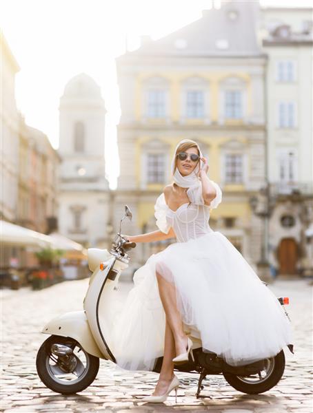 عروس با لباس عروس و عینک آفتابی در حال ژست روی اسکوتر