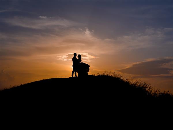 عروس و داماد ایستاده روی تپه در آغوش گرفته اند