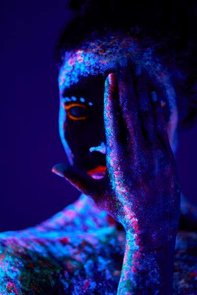 زن جوان سیاه‌پوست با چاپ‌های فلورسنت روی رنگ کیهانی پوست که روی چراغ‌های نئونی می‌درخشد پس زمینه سیاه