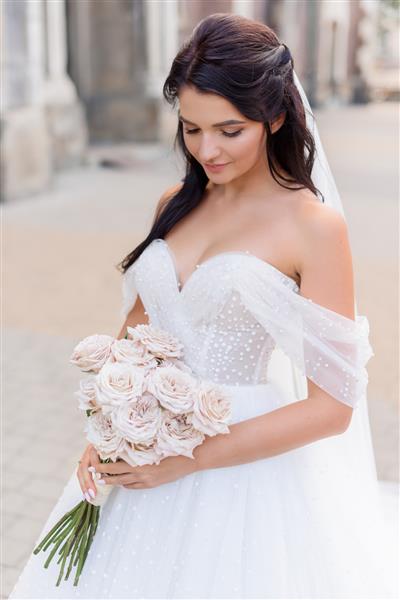 پرتره عروس سبزه شکننده با لباسی زیبا با دسته گل رز در دستانش