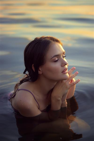 زن جوان زیبا در آب دریاچه با لباس تابستانی در غروب آفتاب پرتره یک دختر خیس عاشقانه در غروب آفتاب گرم زیبایی طبیعی یک زن
