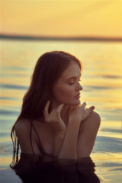 زن جوان زیبا در آب در غروب آفتاب زن مو بلند زیبایی طبیعی در دریاچه