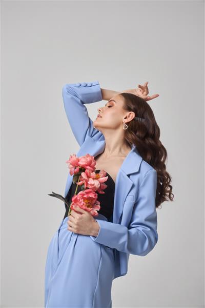 زن مد با کت و شلوار آبی با گل های صورتی زیبایی چهره استودیو هنری پرتره یک زن جوان در زمینه سفید آرایش صورتی