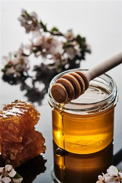 یک شیشه عسل با لانه زنبوری و یک چوب