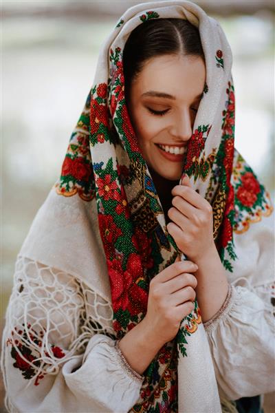 دختر جوان با لباس سنتی قومی با شنل گلدوزی شده روی سرش لبخند می زند
