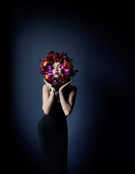 دایره رنگارنگ ساخته شده از گل های تازه روی صورت دختر زیبا زنی با لباس تنگ مشکی در زمینه آبی تیره