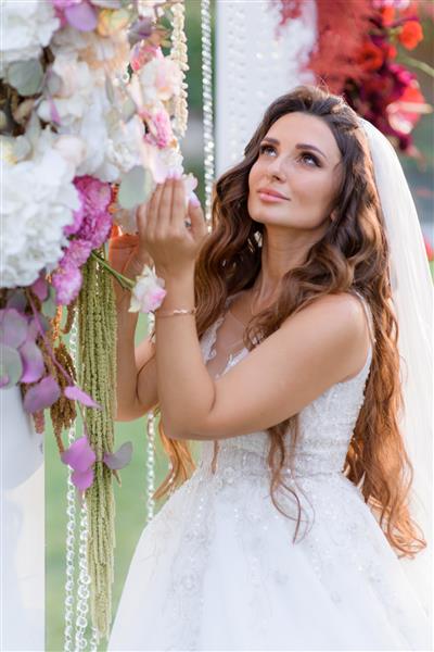 عروس سبزه مو بلند زیبا با لباس عروس در نزدیکی طاق عروسی گلدار