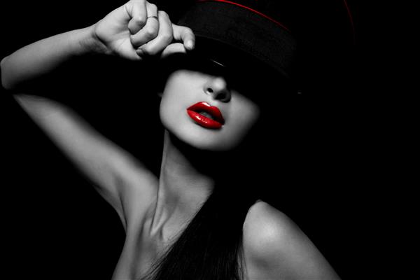 پرتره شیک و جذاب از زن جوان سکسی زیبا با لب های قرمز روی پس زمینه مشکی با کلاه