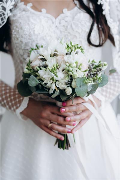 عروس دسته گل زیبای عروسی از گل های سفید و اکالیپتوس را در دست گرفته است