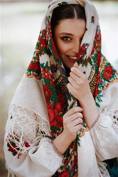زن زیبا با لباس سنتی قومی با شنل گلدوزی شده روی سرش در حال لبخند زدن