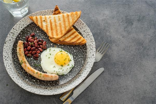 صبحانه کامل انگلیسی سنتی با تخم مرغ سرخ شده سوسیس و لوبیا روی خاکستری نمای بالا