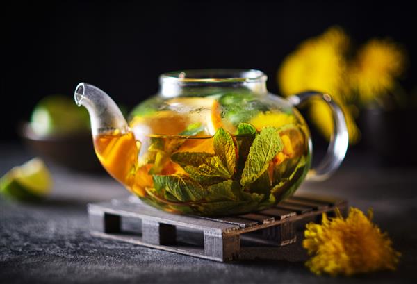 قوری شیشه ای با چای گیاهی میوه ای ترکیب تبلیغاتی چای با پرتقال نعناع خولان دریایی و گیاهان
