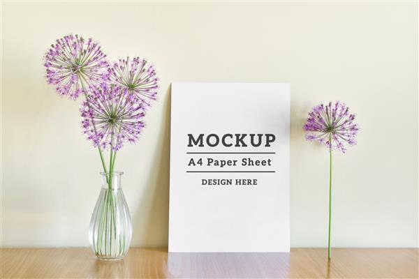 ماکت psd قابل ویرایش با ورق کاغذ A4 ایستاده و گل های تابستانی بنفش روی سطح چوبی