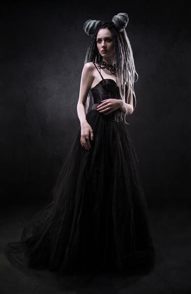 زنی با ترس و لباس گوتیک سیاه که روی پس زمینه تیره ژست گرفته است