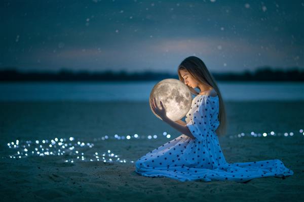 دختر زیبا و جذاب در ساحل شبانه با شن و ماسه و ستاره ماه را در آغوش می گیرد عکاسی هنری