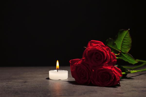 گل رز قرمز زیبا و شمع روی میز در برابر پس زمینه سیاه نماد تشییع جنازه