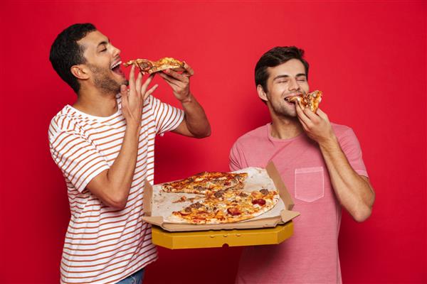 تصویر یک دوست جوان خوشحال خوش تیپ که روی پس زمینه دیوار قرمز جدا شده و در حال خوردن پیتزای بزرگ است