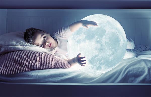 دختر کوچکی که ماه را در دست گرفته در حالی که در رختخواب دراز کشیده است