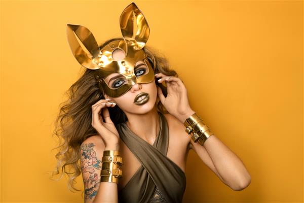 دختر زیبا با ماسک خرگوش چرمی طلایی شیک در زمینه زرد مفهومی برای مهمانی