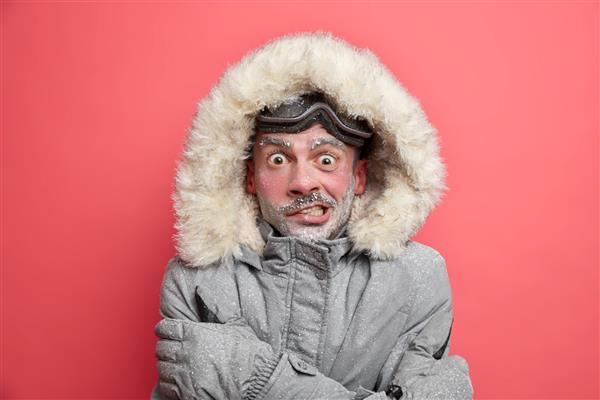 مرد یخ‌زده از سرما می‌لرزد چهره‌ای قرمز پوشیده از ریش یخ‌زده ژاکتی با کلاه می‌پوشد که باید در طول ژست‌های سفر زمستانی روی پس‌زمینه مرجانی گرم شود هوای سرد دمای پایین