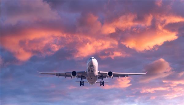 هواپیما در غروب خورشید در آسمان رنگارنگ پرواز می کند منظره با هواپیمای مسافربری سفید آسمان بنفش با ابرهای صورتی هواپیما در حال فرود است سفر کاری هواپیمای تجاری مسافرت رفتن نمای هوایی مفهوم