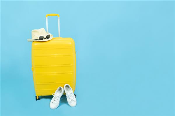 تعطیلات تابستانی تعطیلات و مفهوم سفر چمدان یا کیف چمدان زرد کفش های کتانی سفید و عینک آفتابی مد روز روی کلاه آفتابی جدا شده در پس زمینه آبی با فضای کپی