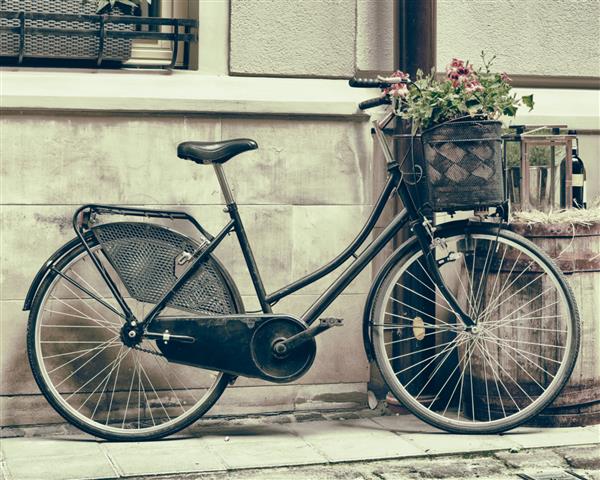 عکس سبک قدیمی از دوچرخه قدیمی که گل ها را به عنوان تزئین حمل می کند