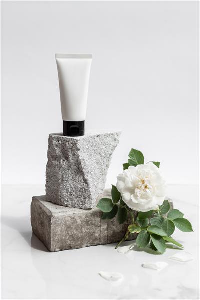 لوله سفید کرم یا لوسیون بدن روی یک تکه سنگ روی زمینه سفید طبیعی با گل سفید رز لوازم آرایشی ارگانیک مراقبت از پوست زیبایی اسپا درمانی مفهوم بهداشت و درمان