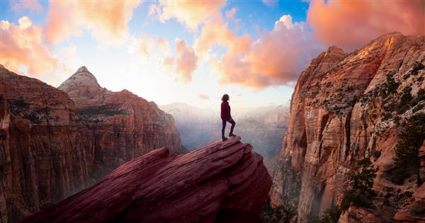 زن ماجراجو در لبه یک صخره در حال تماشای منظره ای زیبا در دره در هنگام غروب پر جنب و جوش است در پارک ملی Zion یوتا ایالات متحده گرفته شده است پانورامای ترکیبی آسمان