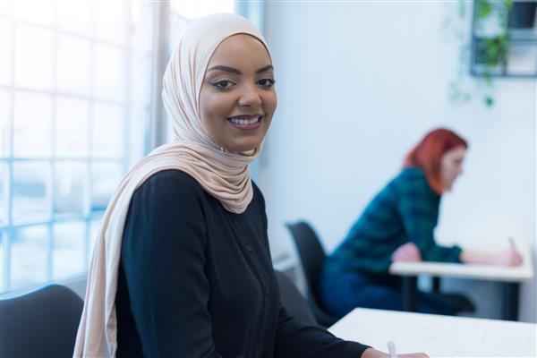 همکاران جوان مدرن در حال ارائه در مورد استراتژی های بازاریابی جدید زن مسلمان آفریقایی زن به دوربین نگاه می کند و لبخند می زند