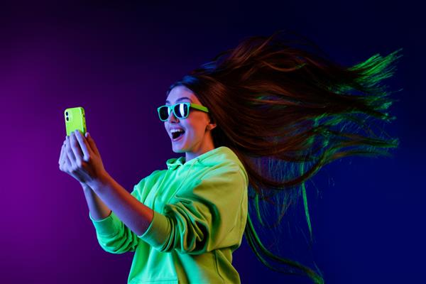 عکس زن جوان حیرت‌زده به‌نظر می‌رسد که موی مگس اینترنتی سریع با تلفن همراه جدا شده روی پس‌زمینه نئون رنگارنگ