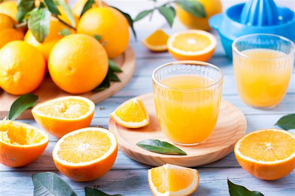 دو لیوان آب میوه تازه میوه گیر و پرتقال تازه رسیده روی میز چوبی آبی رنگ آب پرتقال تازه درست کردن نمای بالا