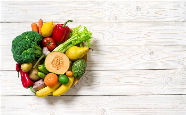 بشقاب با سبزیجات و میوه ها روی میز چوبی غذای سالم نمای بالا