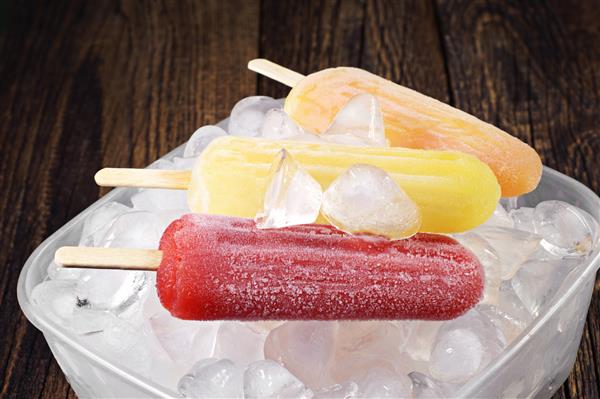 بستنی میوه ای رنگارنگ در یک کاسه یخ روی میز چوبی